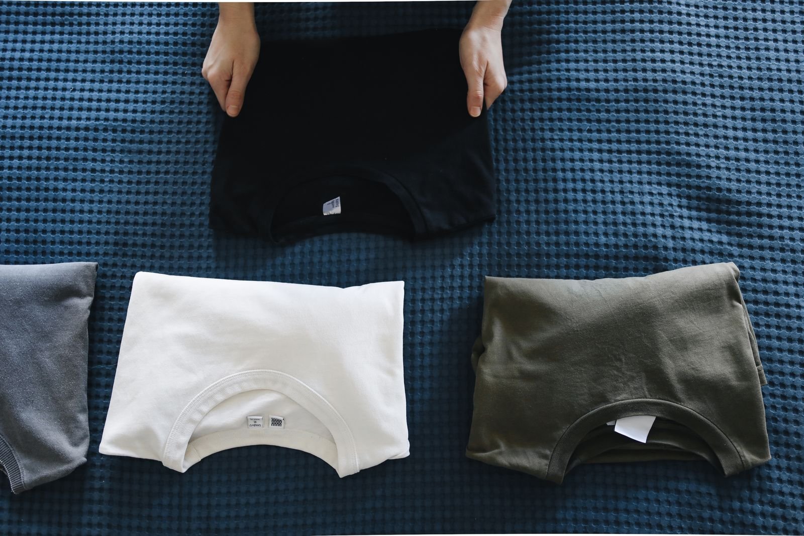 Mani che piegano alcune t-shirt usate, ordinate per colore